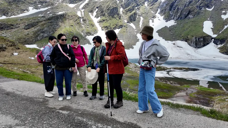 Travellers pausing together beside Bâlea Lake, with snow still on the slopes