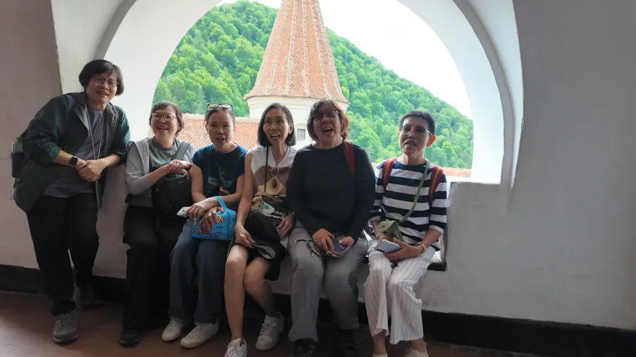 A group of travellers sitting in a window arch at Bran Castle, smiling