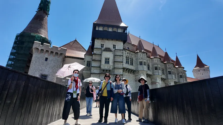A group of travellers with umbrellas walking up to Corvin Castle in Hunedoara