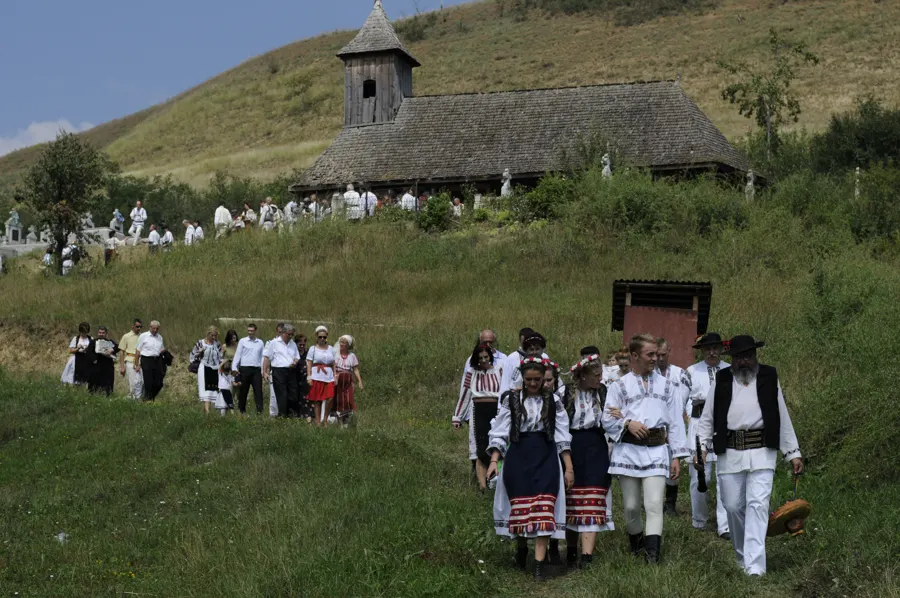 Villagers in traditional dress walking up a hillside to a wooden church